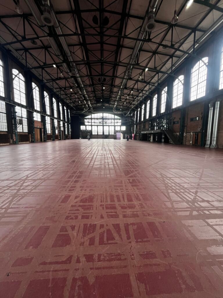 Weite, leere Industriehalle im E WERK Saarbrücken mit rotem Boden, Stahlträgern und großem Rundbogenfenster