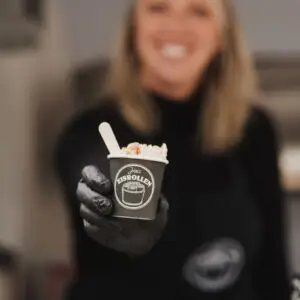 Jessica von Jessi's Eisrollen reicht einen Becher frisch zubereiteter Eisrollen